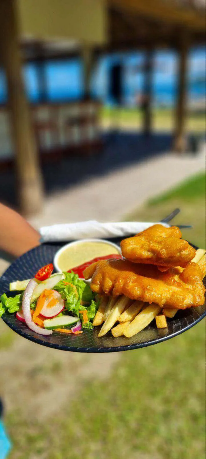 Plate of crispy fish and chips with fresh salad and sauces, served outdoors at a Fiji beach resort.
