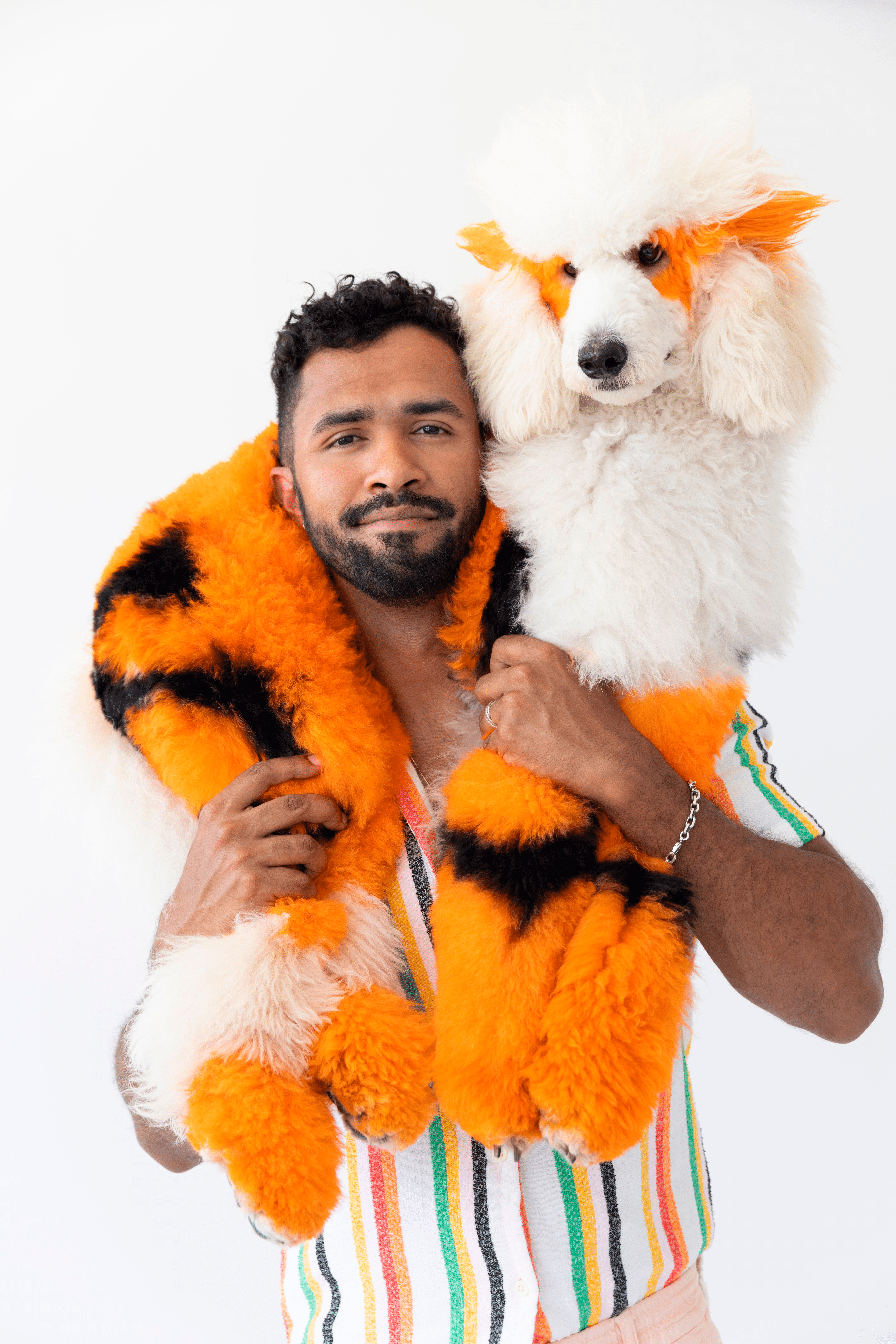 Vibrant portrait of Gabriel Feitosa holding a creatively styled poodle with orange and black accents to express bold artistry and joyful luxury in pet grooming.