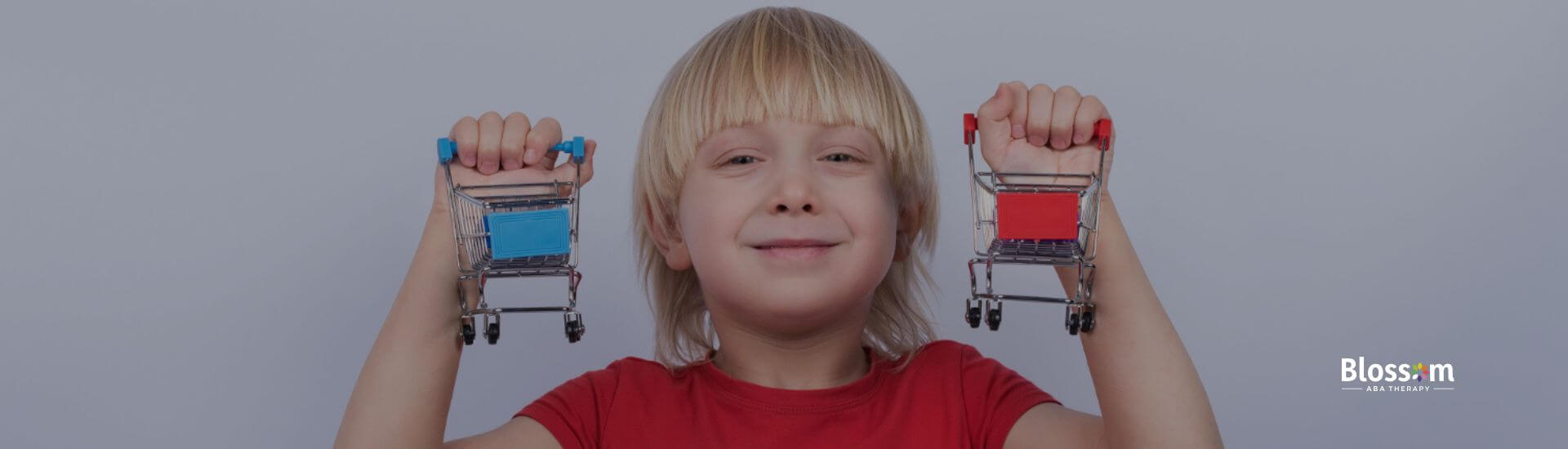 A boy with high-functioning autism smiles while holding two small shopping carts.