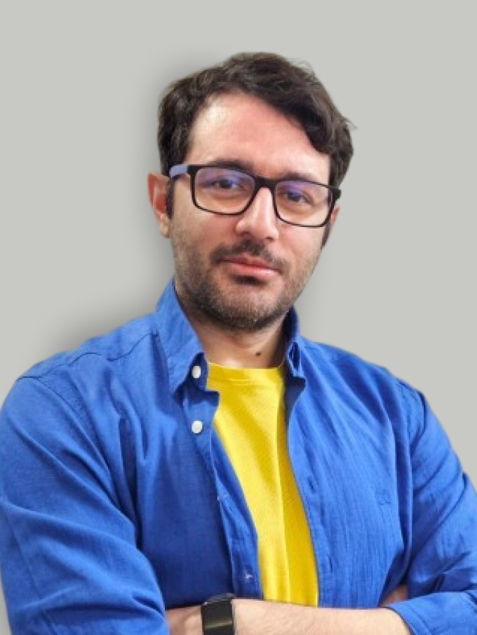 A man with glasses and a brown shirt, crossing his arms.