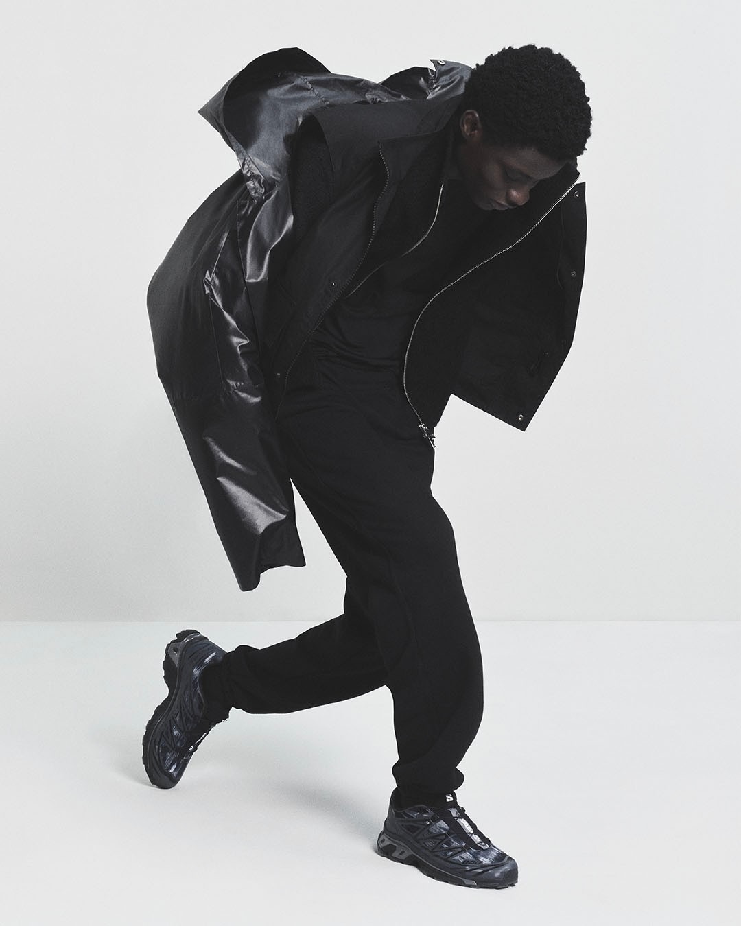 Un homme vêtu de noir esquisse un pas de danse en baskets Salomon