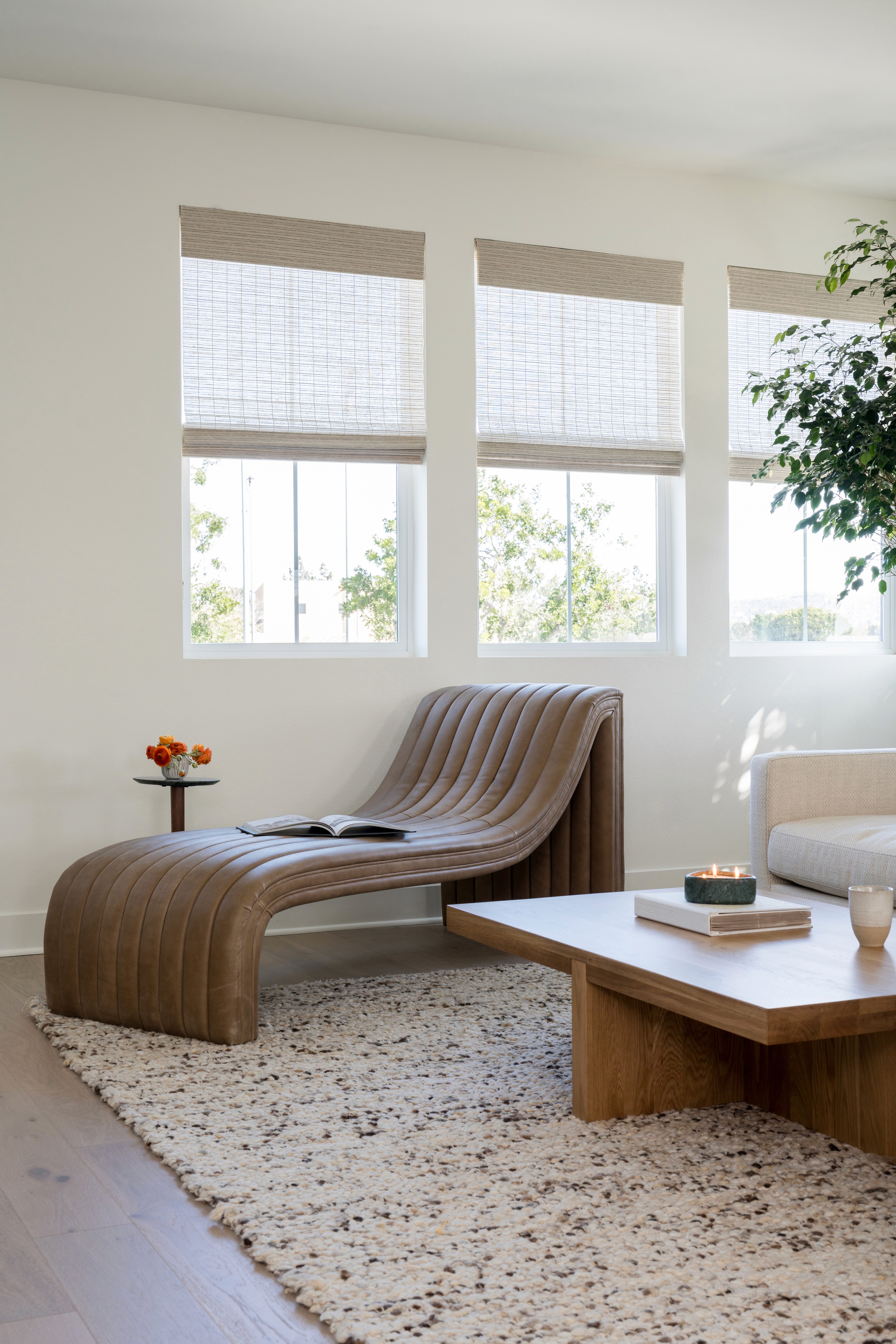 Modern faux leather lounge, woven area rug, and light wood coffee table with ceramic bowl, large coffee table book, and green marble candle