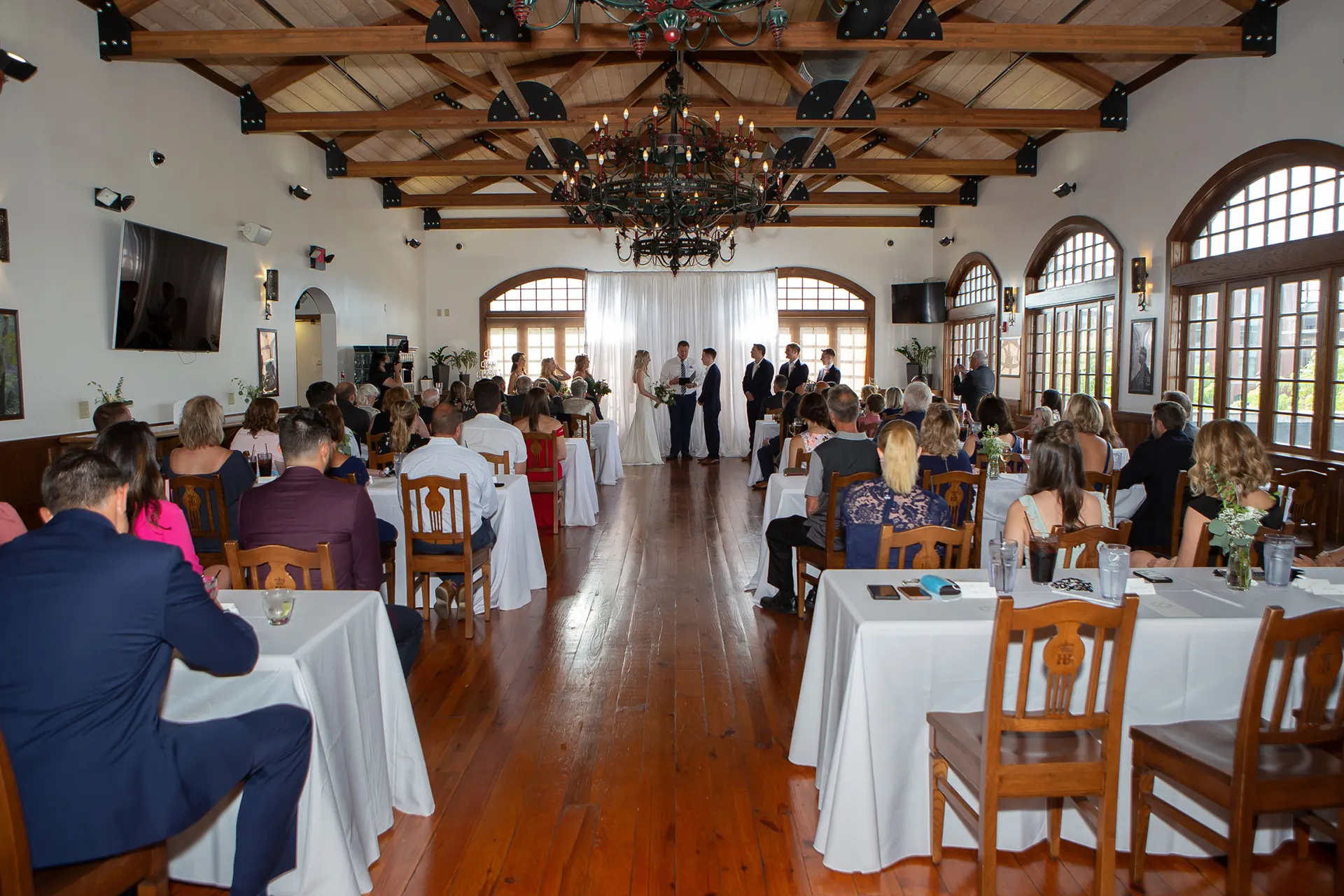 Event room with arched windows, wood beams and a chandelier set for a ceremony
