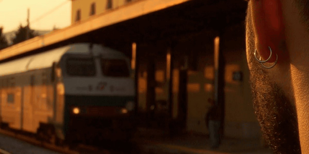Man with earrings at sunset watching a train arrive at Battipaglia station, symbolizing Moicano Mc’s hip-hop journey.