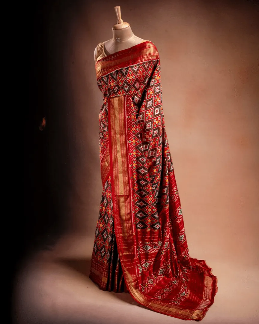 An orange Ikat saree from That Saree Shop draped on a mannequin, displaying its handwoven geometric patterns and rich traditional craftsmanship in vibrant hues.
