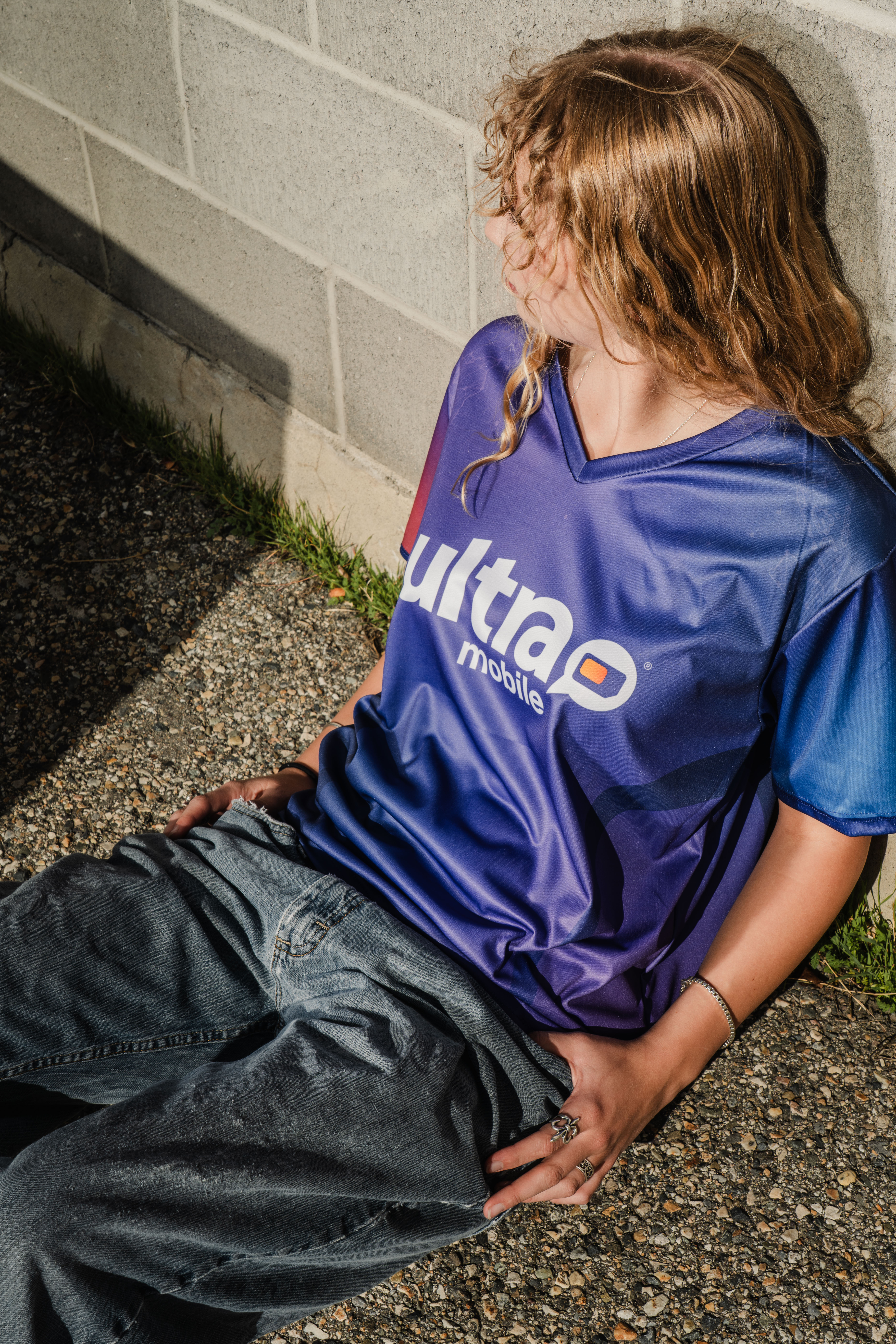 Ultramobile jersey on model that is sitting on asphalt leaning up against cinderblock.