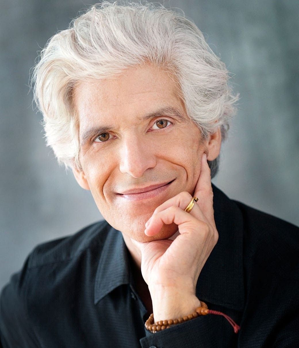 Confident man standing in a greenhouse surrounded by lush green plants, wearing a beige shirt and neutral-toned outfit.