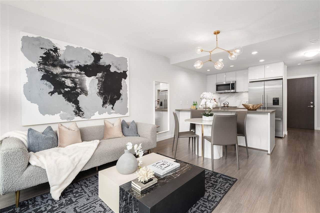 A modern living room with a couch, coffee table, and an open kitchen area, featuring abstract wall art.