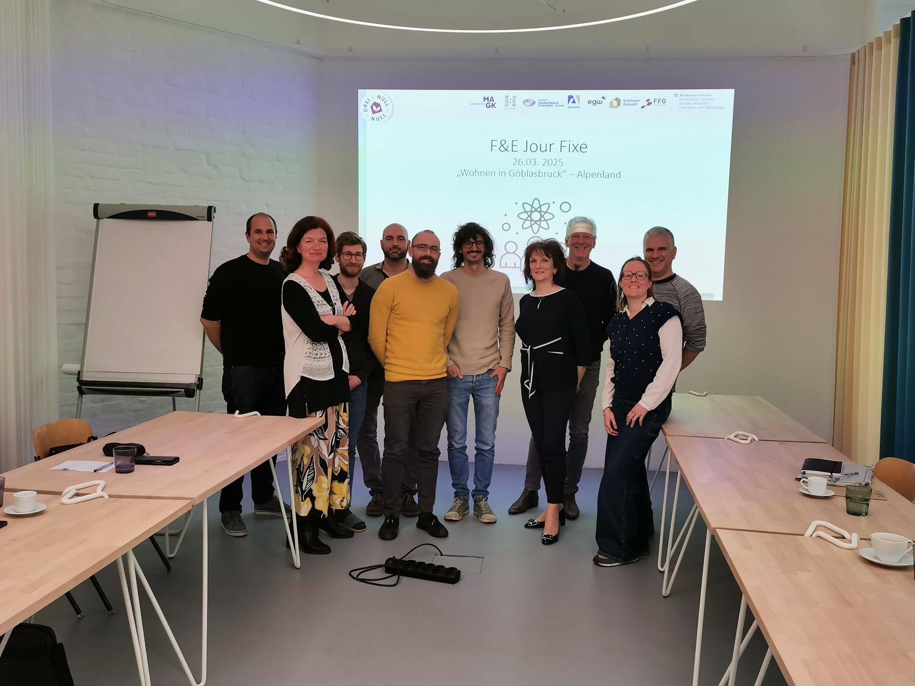 Group of ten professionals posing in a modern meeting room beneath a presentation screen.