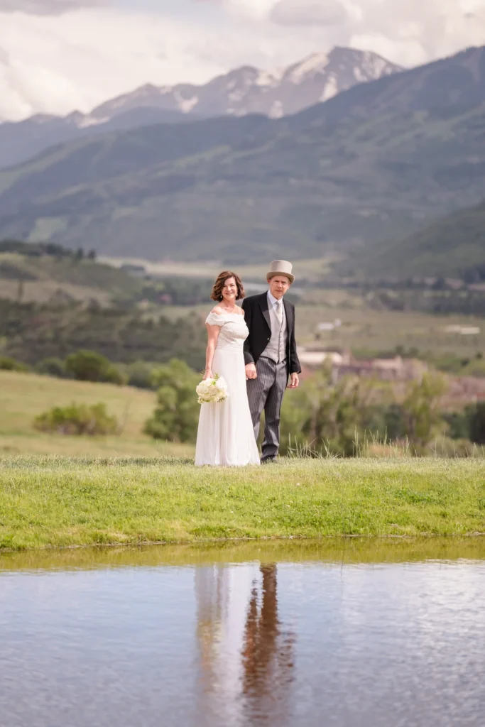 Newlyweds standing beside a pond with mountains behind them