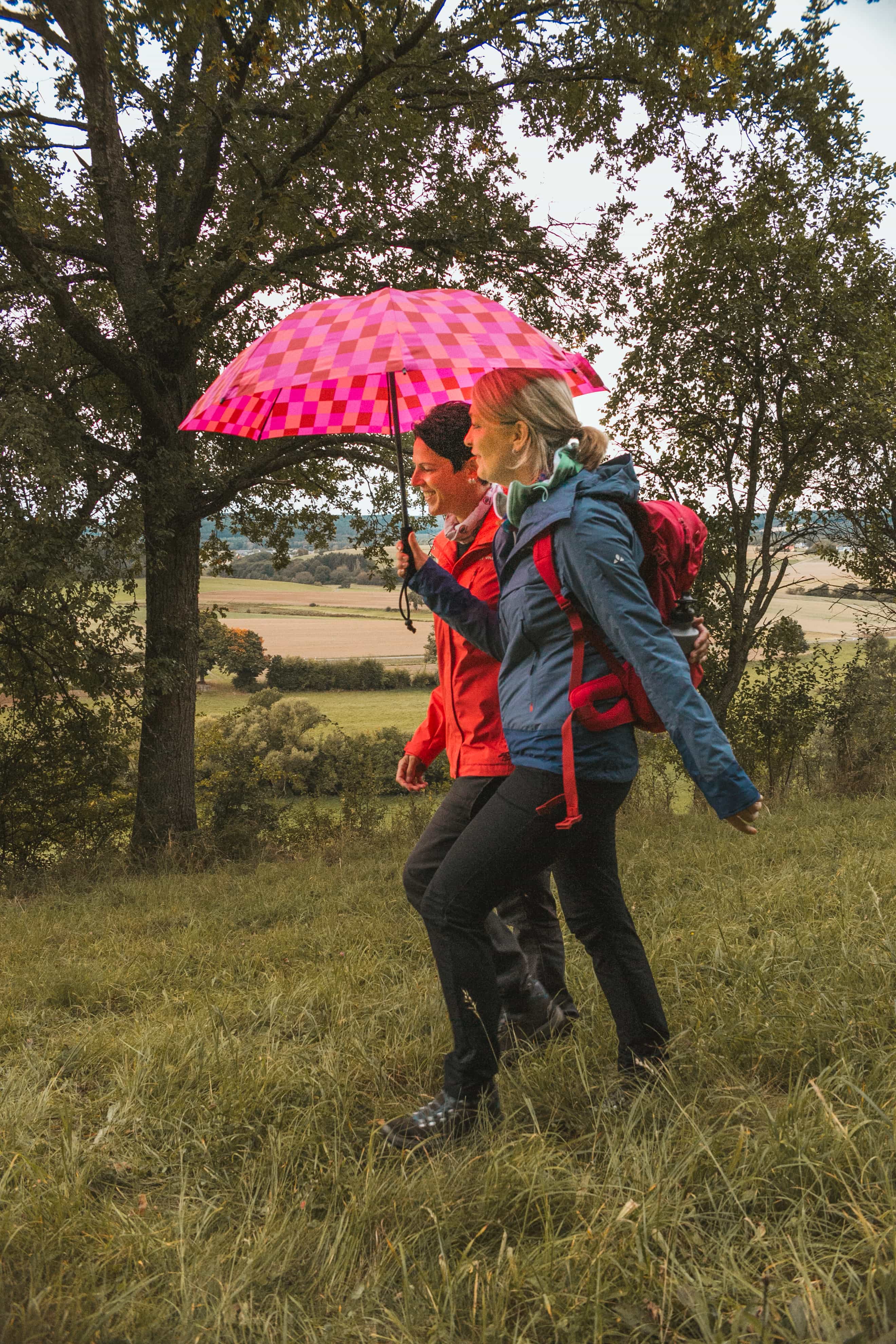 two women are walking under a pink umbrella