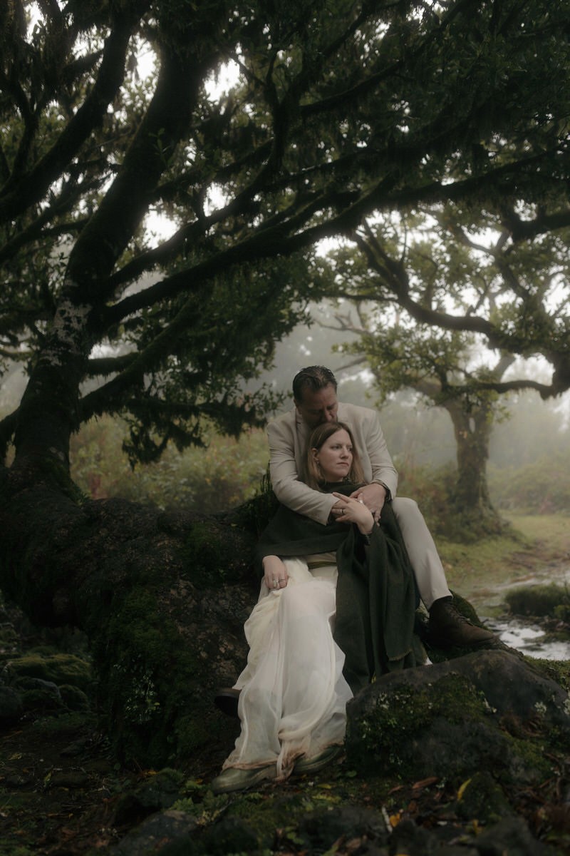 elopement couple sitting beneath laurel tree in misty fanal forest