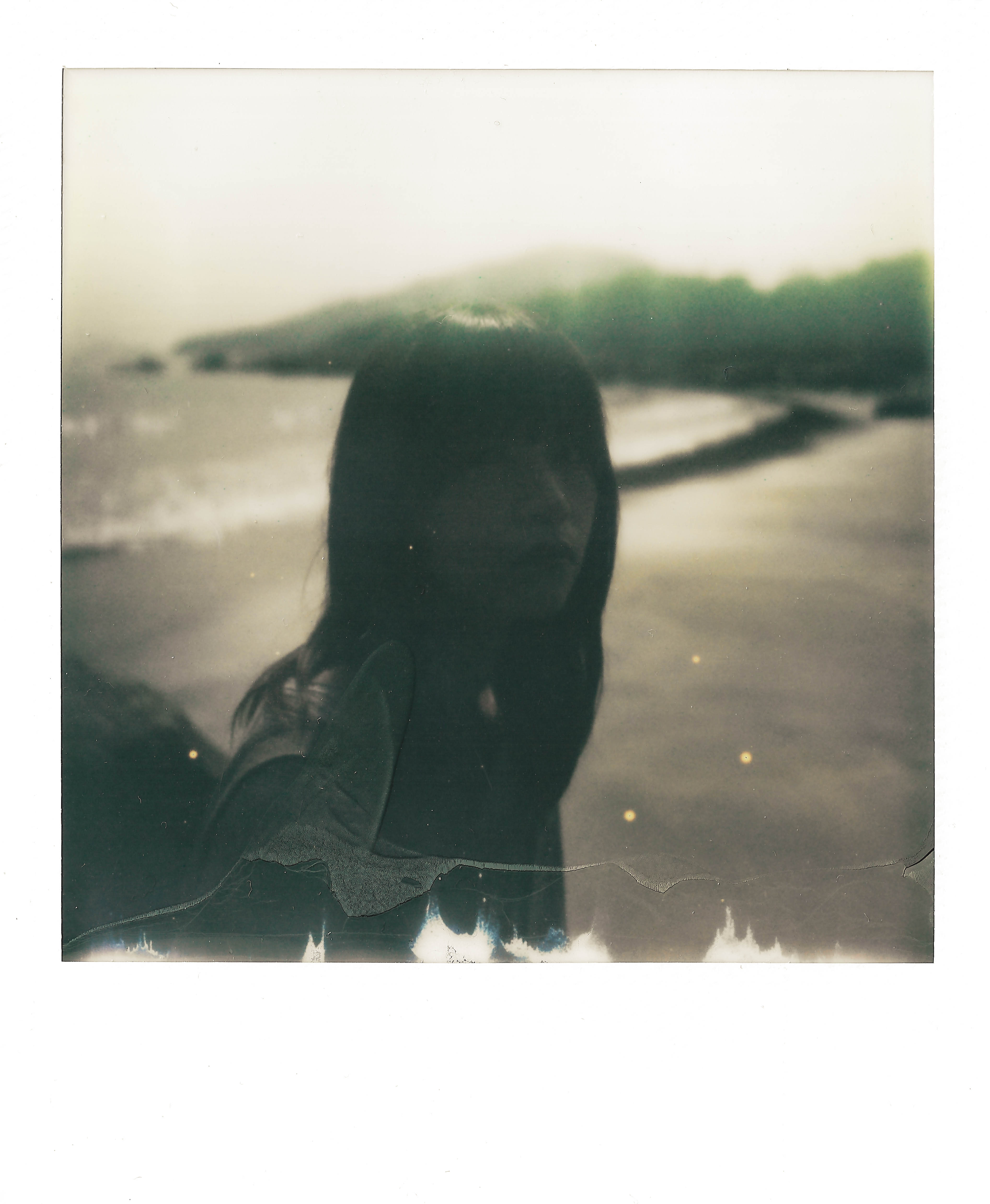 Alice in adulthood sitting on beach looking towards to the instant camera