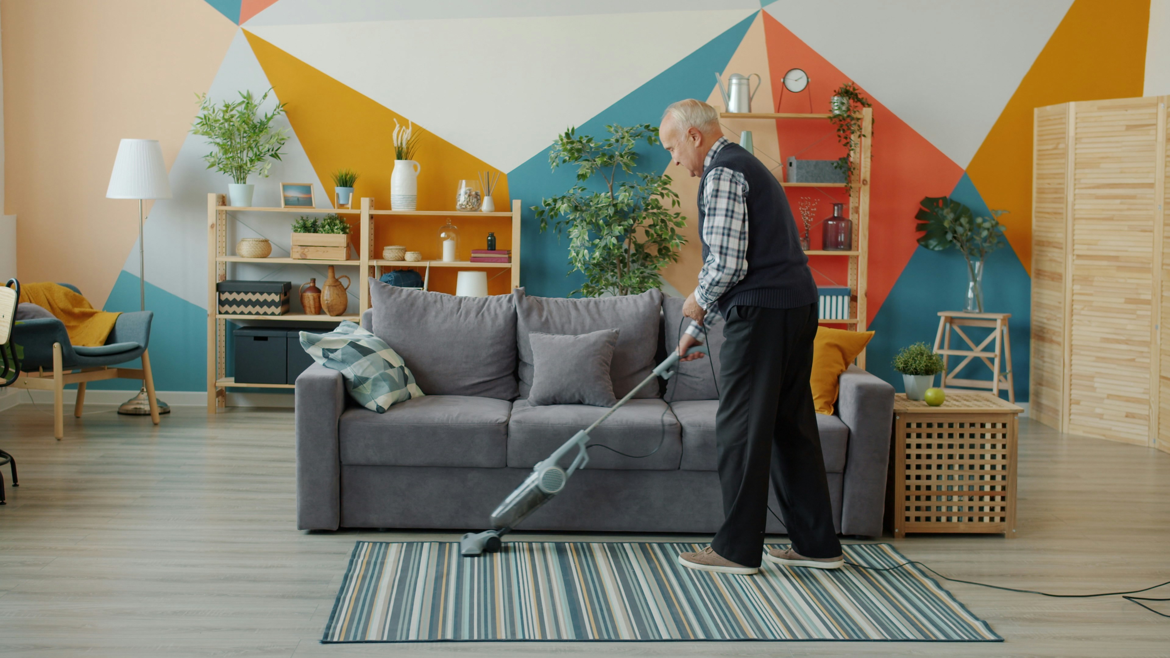 Elderly woman vacuuming a colorful living room floor