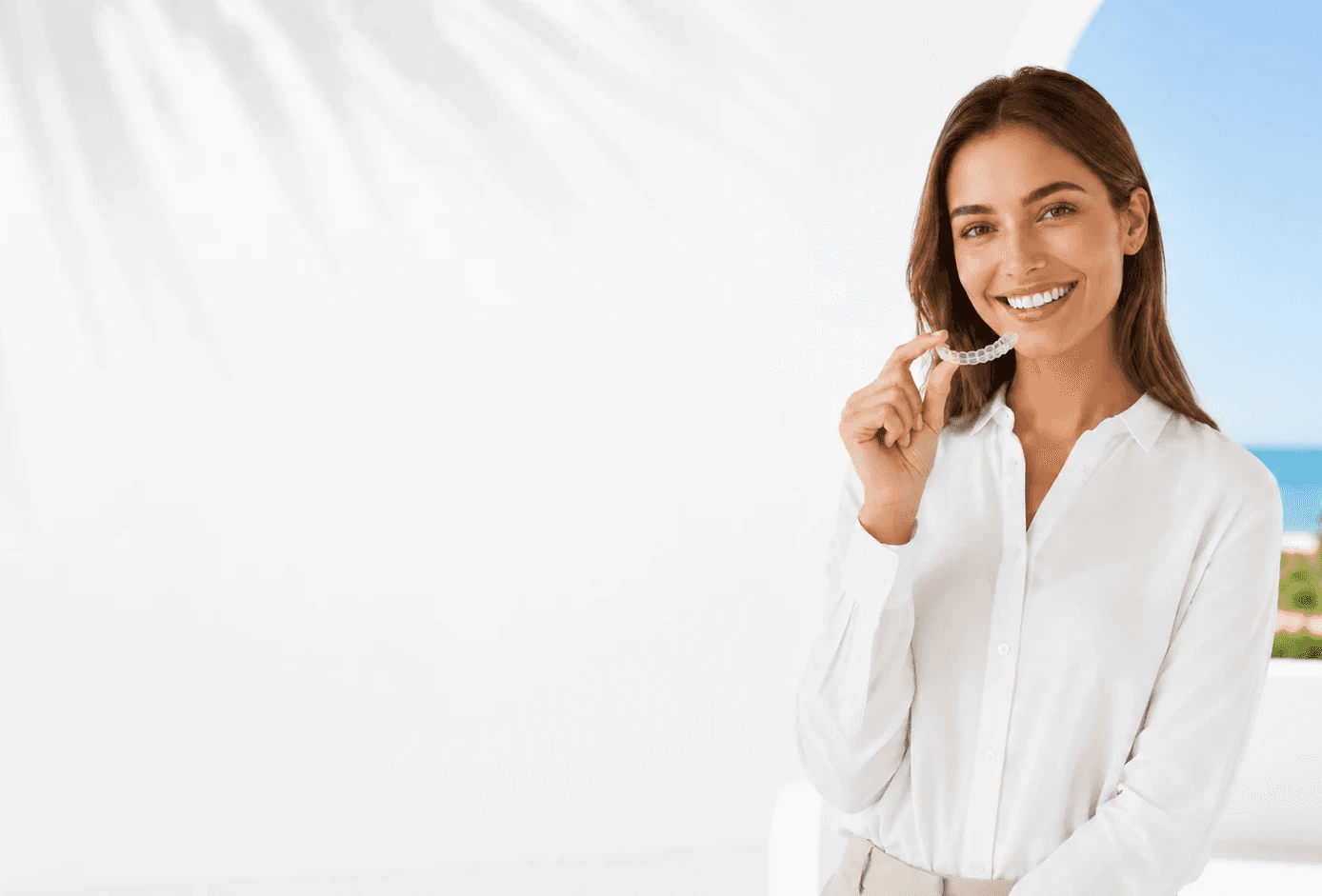 Smiling girl in blue shirt inserting Invisalign clear aligners, enjoy the summer offer now at Invisalign Center Dubai.