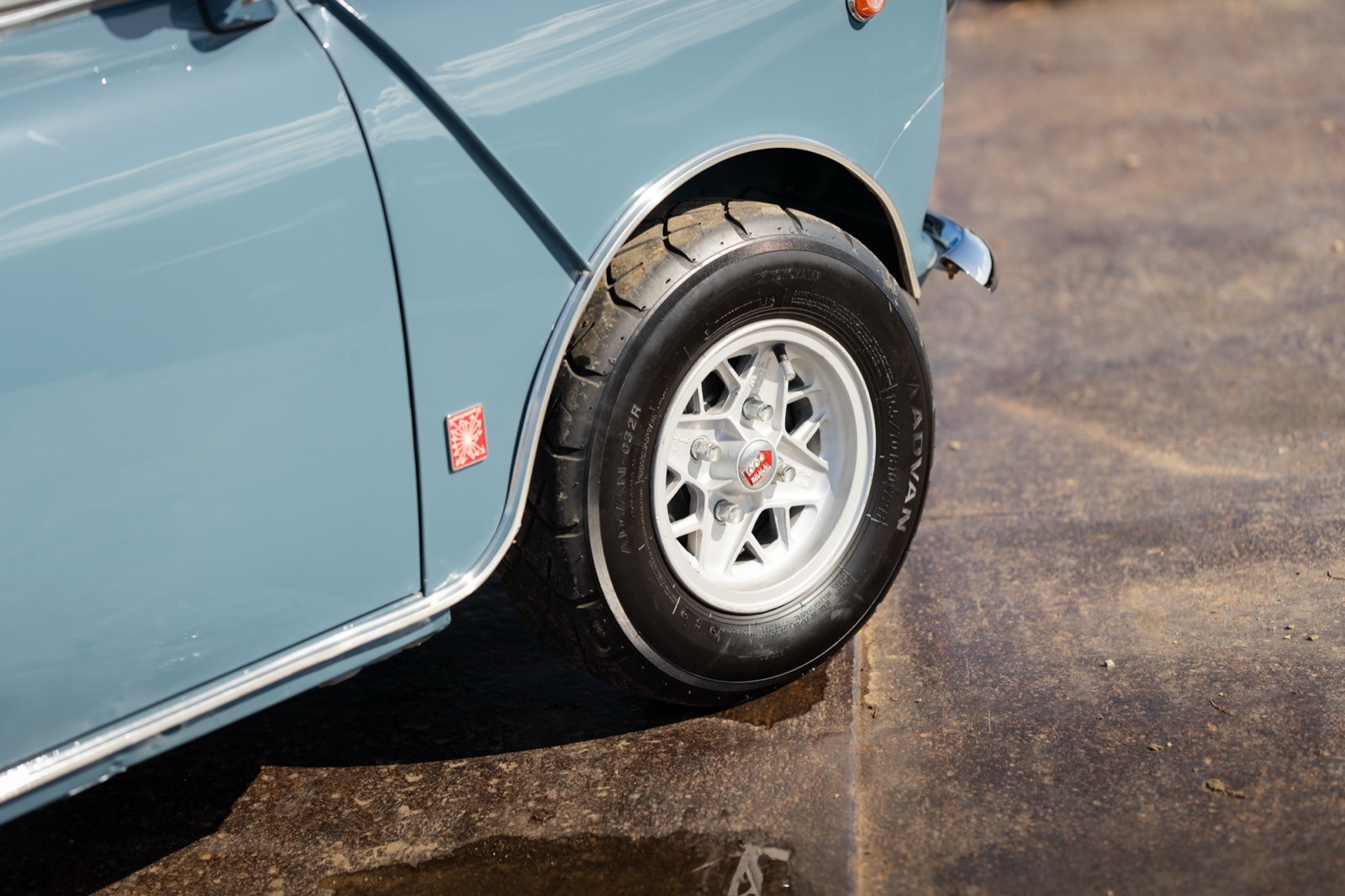 Close-up of the rear wheel and fender of a vintage light blue car, showing details of the tire and rim.