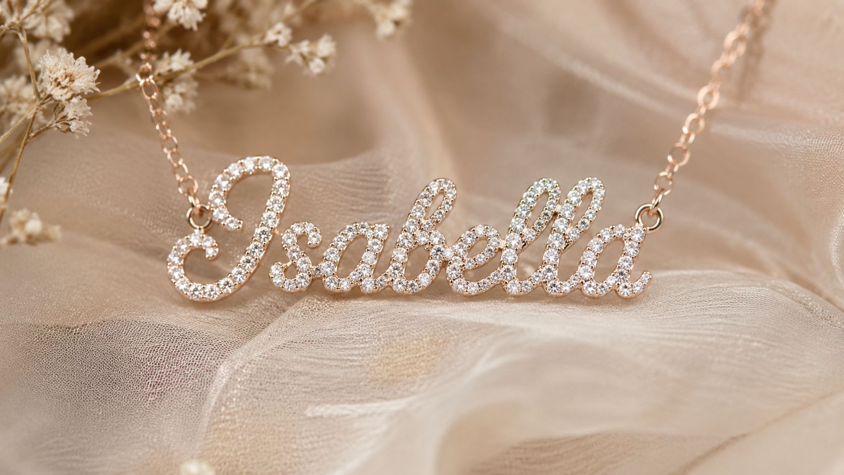 A delicate gold necklace featuring a custom diamond-studded name pendant spelling Isabella, displayed on soft fabric.