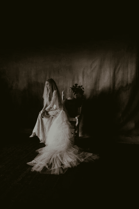 Low-light bridal portrait featuring a bride in a long, flowing gown, bathed in shadows, illustrating the emotional depth and intensity of moody wedding photography.