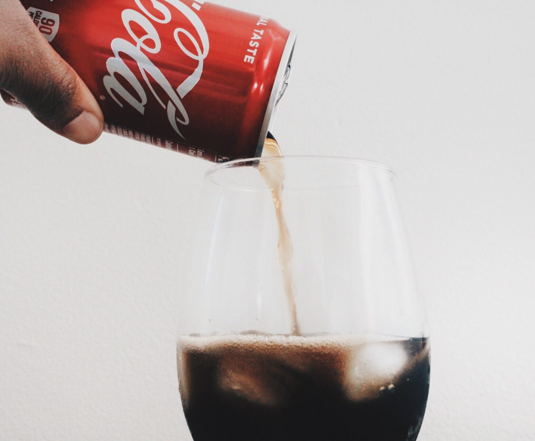 Hand pouring Coca-Cola from a classic red can into a clear glass, highlighting the brand’s iconic product and timeless appeal