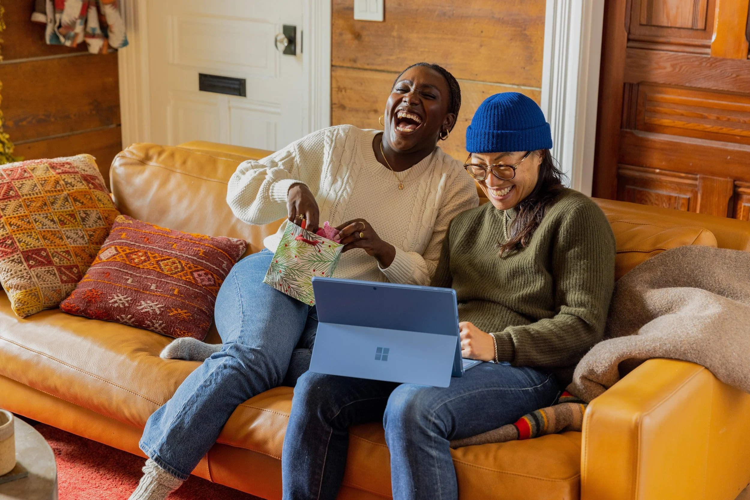 Two people sit on the couch sharing a good time while looking at something on a laptop