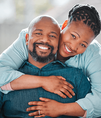 A woman hugs her partner from the back as they face the camera.