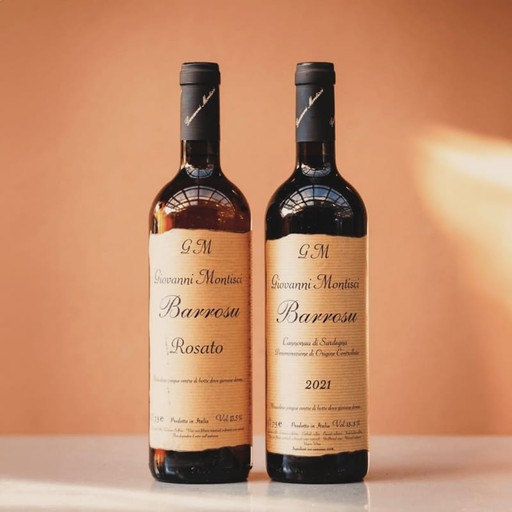 Two bottles of Giovanni Montisci “Barrosu” Cannonau red wine from Sardinia standing on a light surface with a warm background.