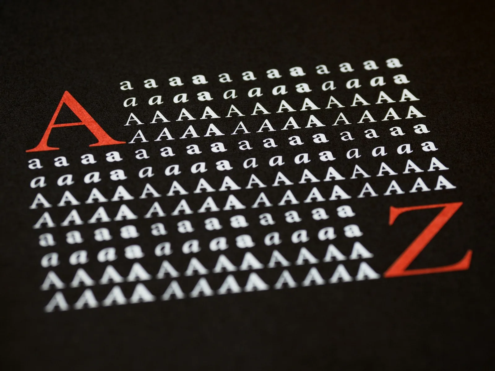 Type specimen printed on black paper, rows of white serif letter A in different weights and italics with a large red A and Z