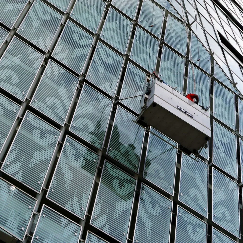 Rope-access gondola cradle inspecting a glass facade, the manual method drone inspection replaces