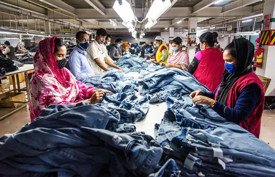 Industrial garment factory with workers inspecting and processing denim jeans on a textile production line. Apparel manufacturing facility showcasing clothing production and quality control operations.