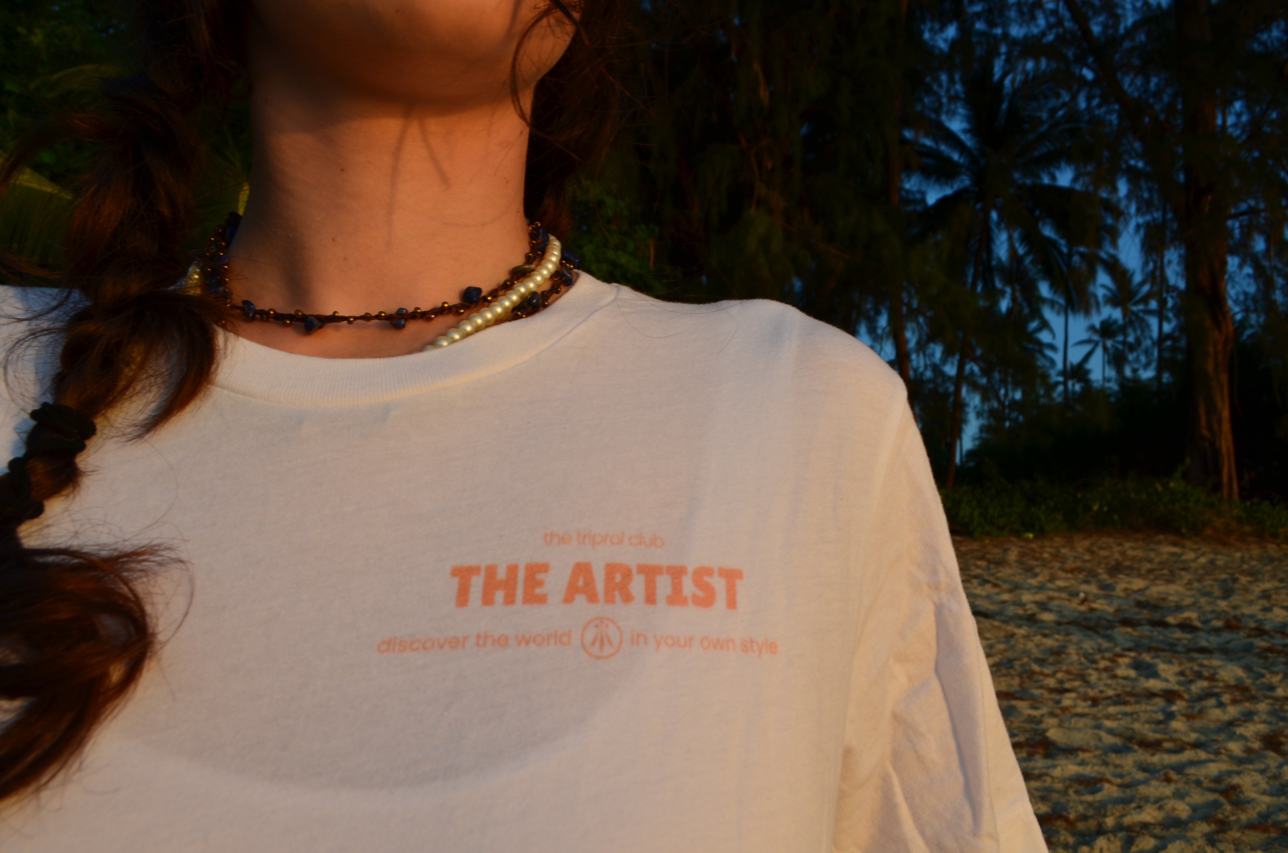 Smiling young woman with long hair standing against a dark green background, holding a finger to her chin.