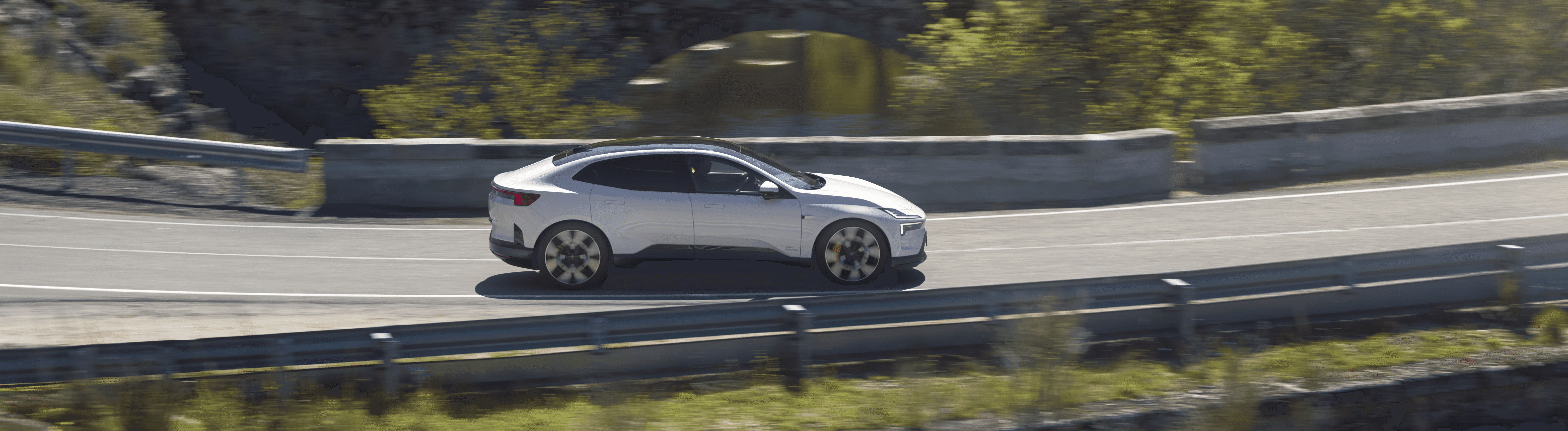 Polestar 4 blanche en conduite sur route de campagne, vue latérale dans un décor verdoyant