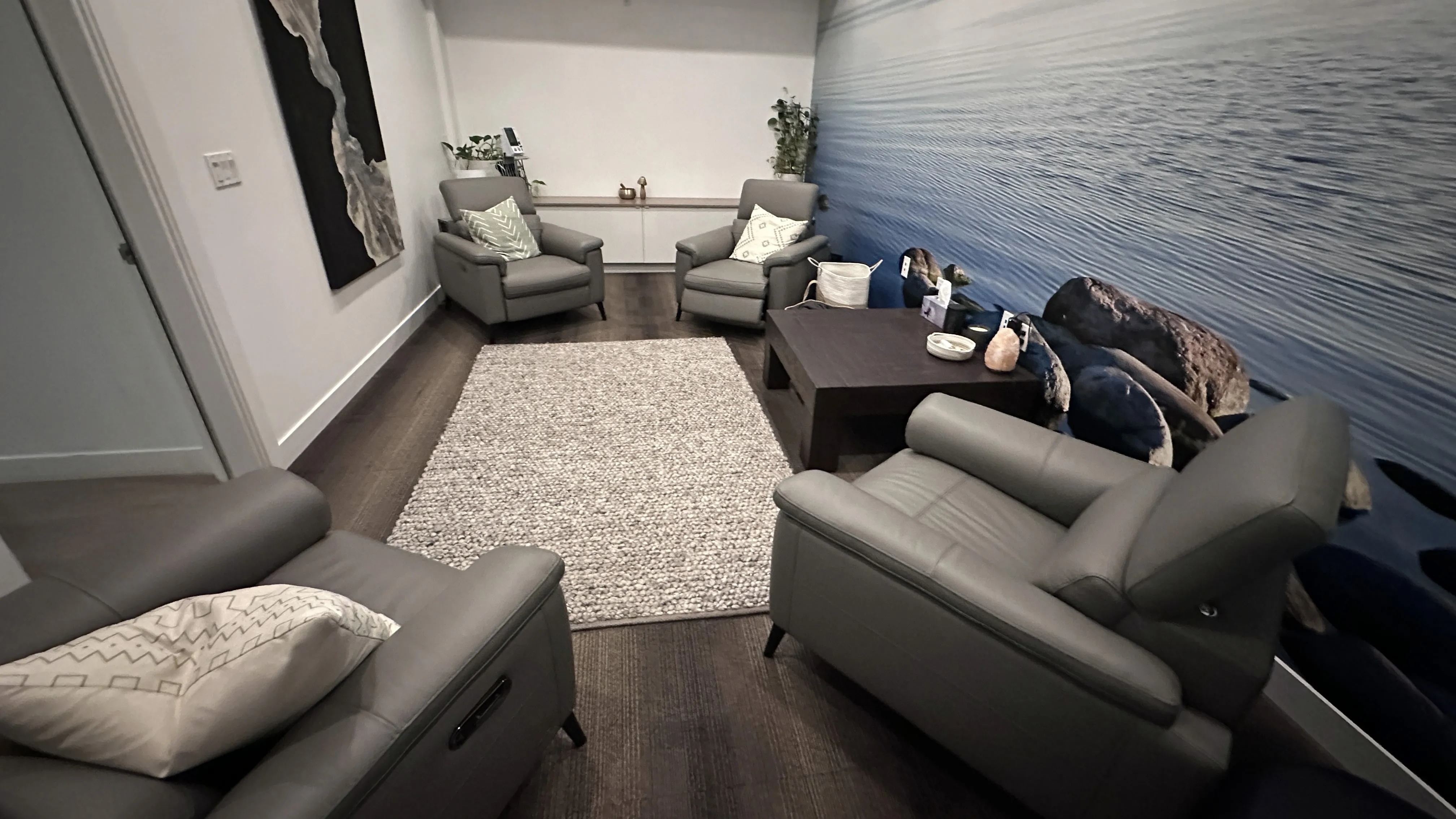 Lounge room with an ocean mural, gray reclining chairs, a coffee table, and a decorative rug