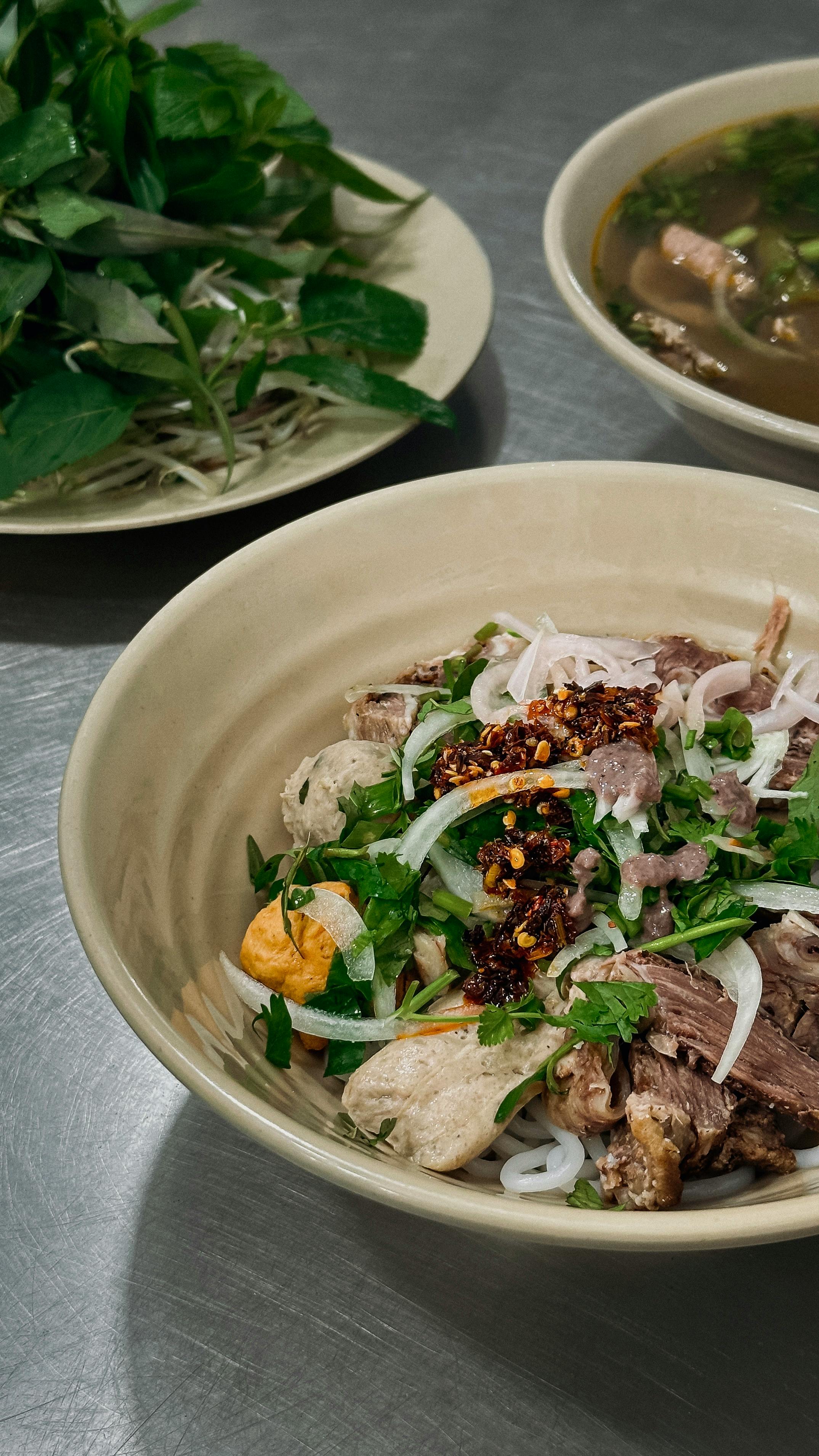 Smiling young woman with long hair standing against a dark green background, holding a finger to her chin.