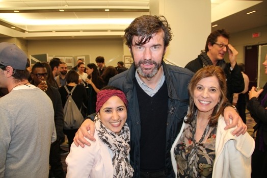 A photo of three people standing in a room among other people.