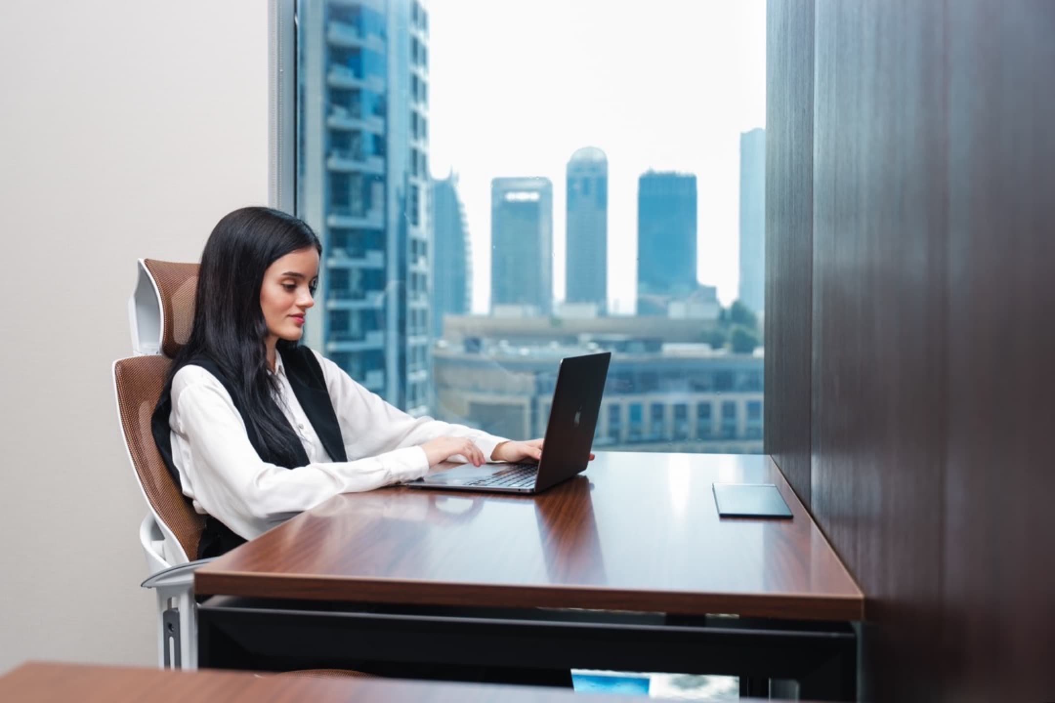 Woman working on a laptop in a Dubai office setting representing mainland license business setup and operations