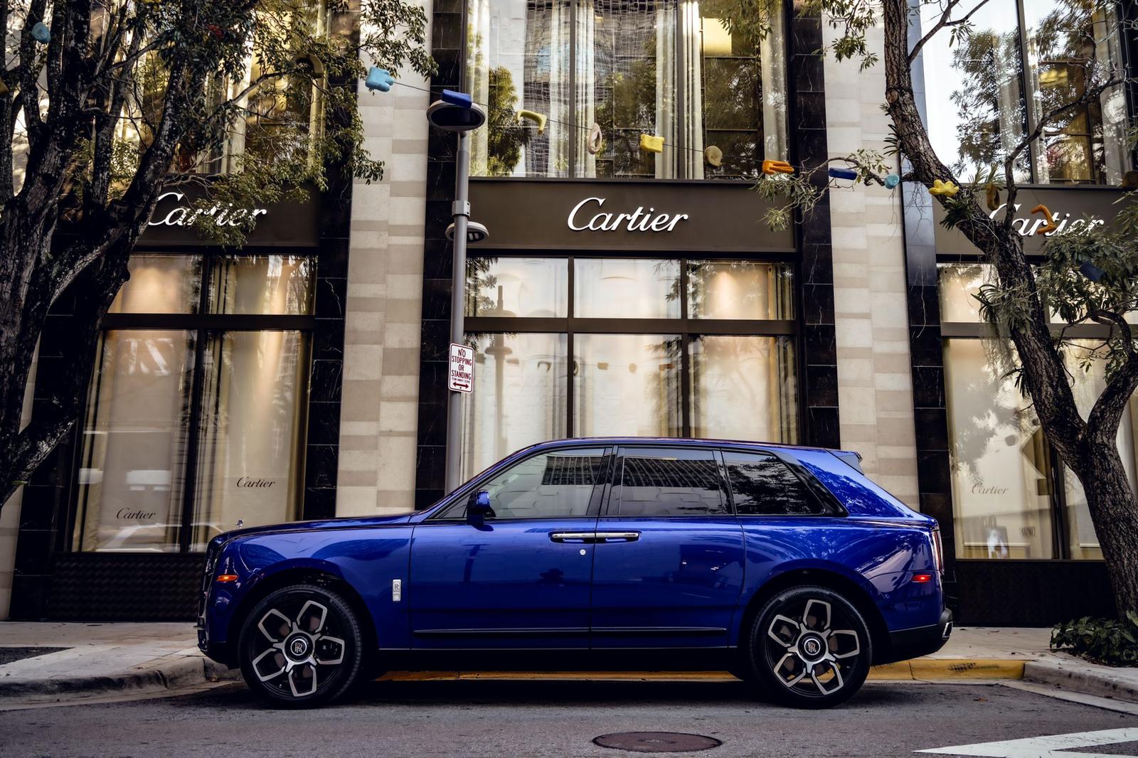 Side profile of blue Rolls-Royce Cullinan SUV showcasing elegant proportions and coach line detail, parked against classic architecture