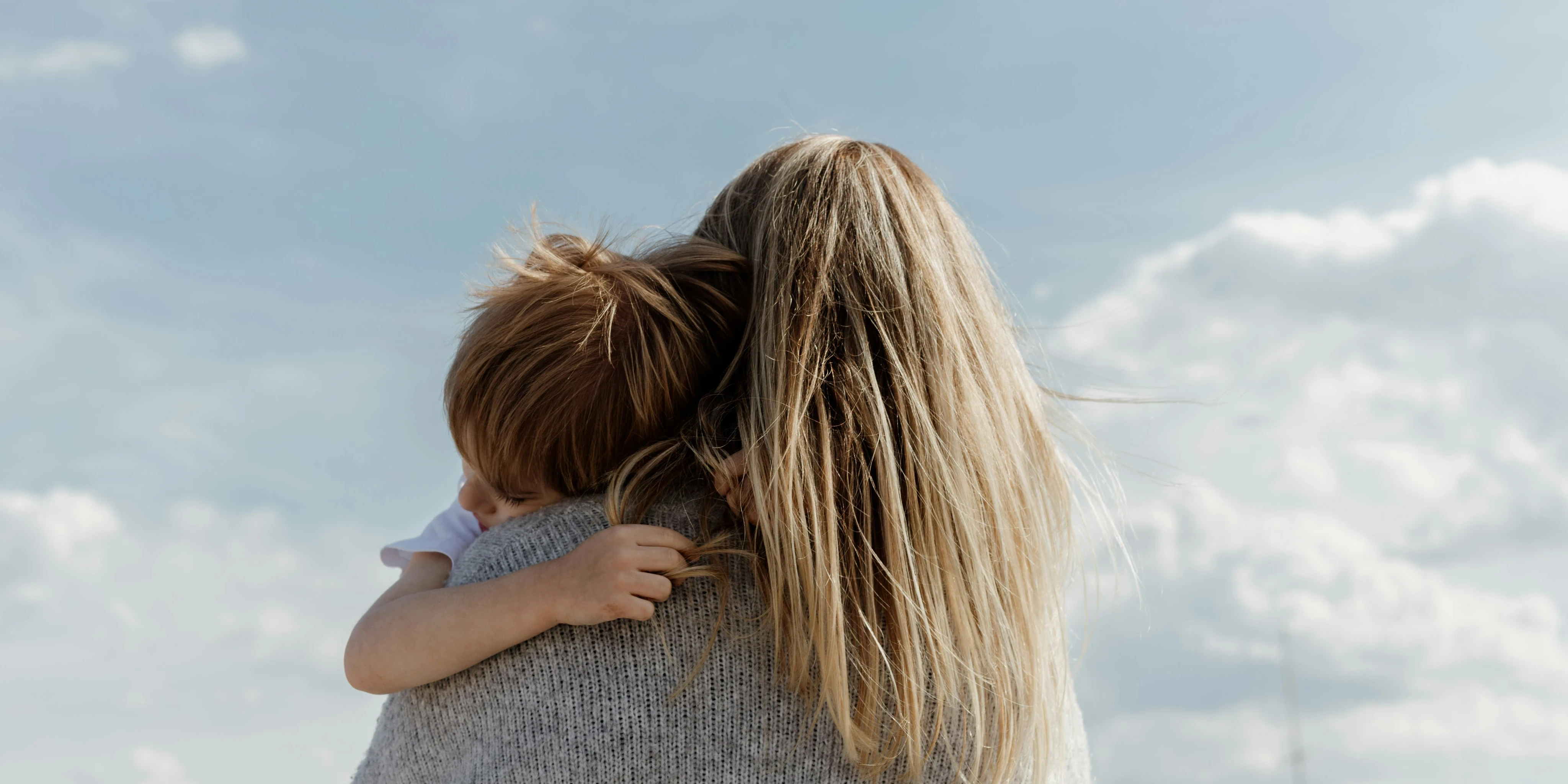 woman holding child from behind against cloudy sky