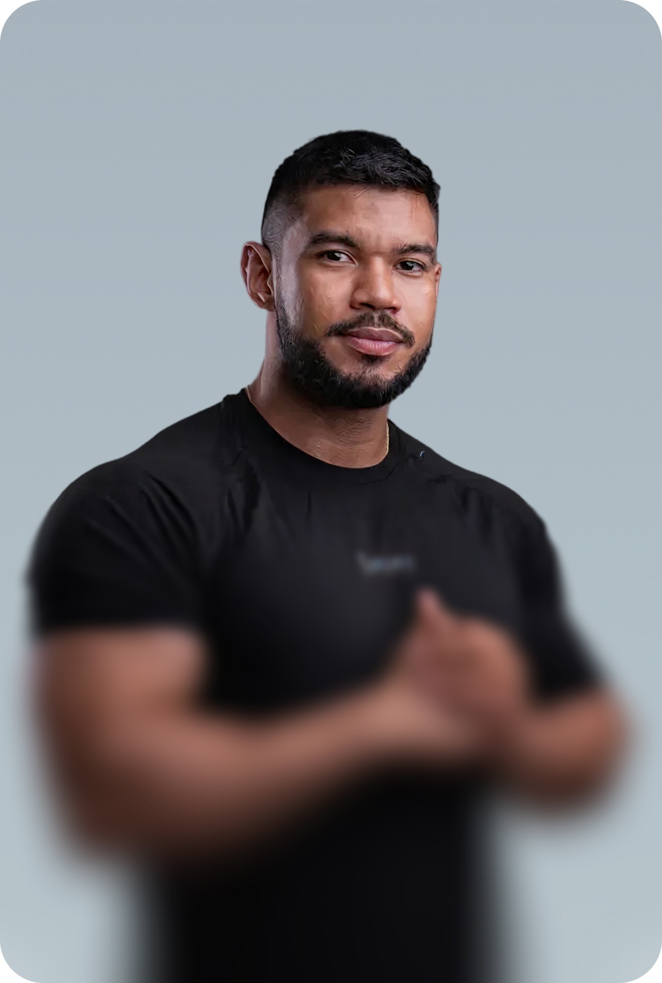 Man in a fitted black polo shirt standing with arms at his sides on a grey background