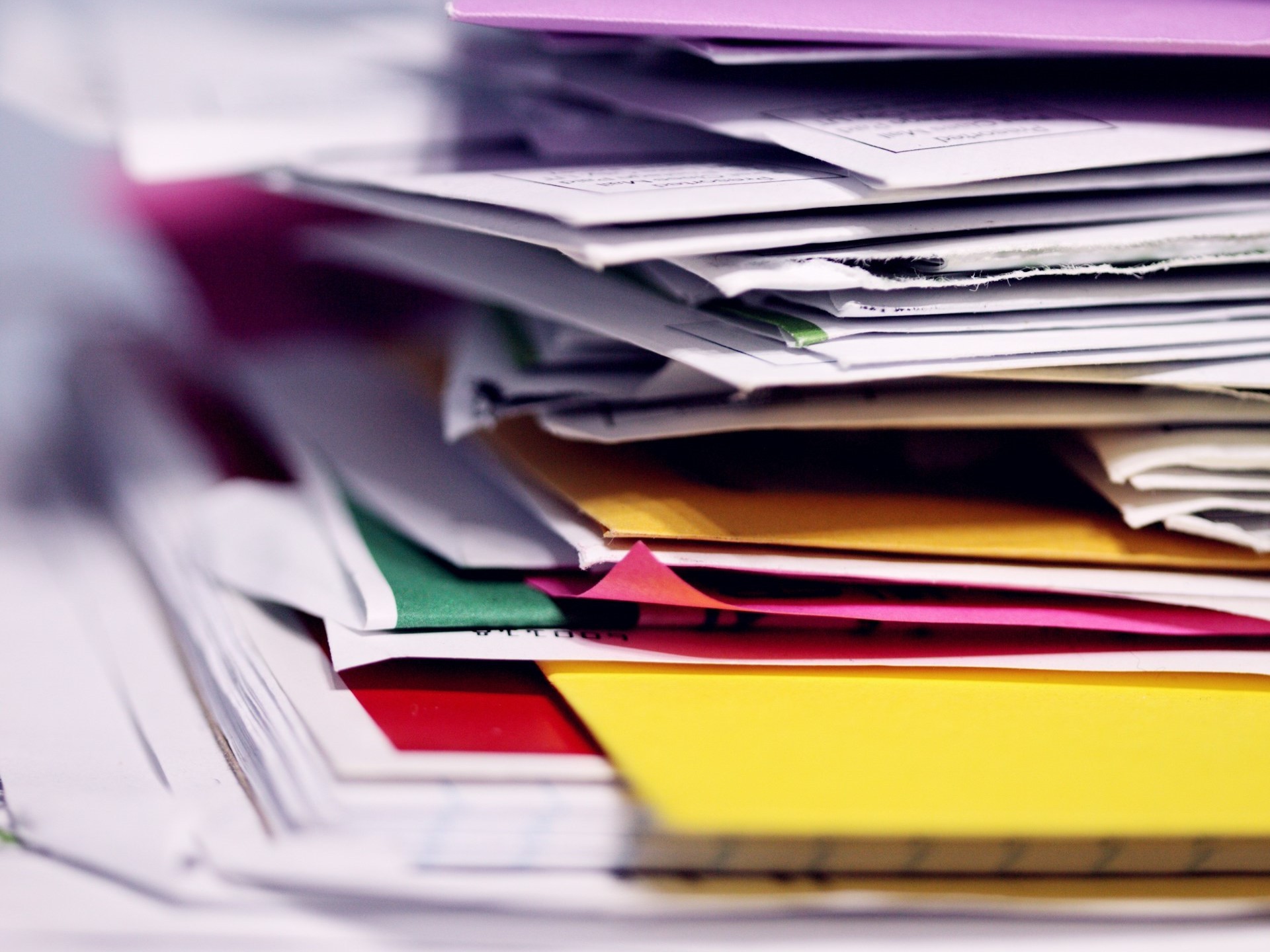 Stack of papers messy on a desk in multiple colors.