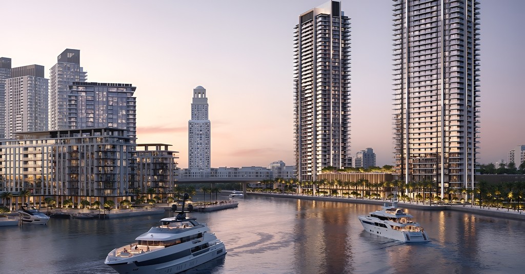 Oceanfront tower of Creek Bay Emaar Properties illuminated by a vibrant sunset, reflecting colors on the water.