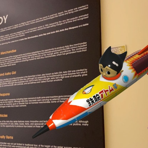 A small figurine of a child in a rocket suit is attached to a yellow wall, next to a text display board.