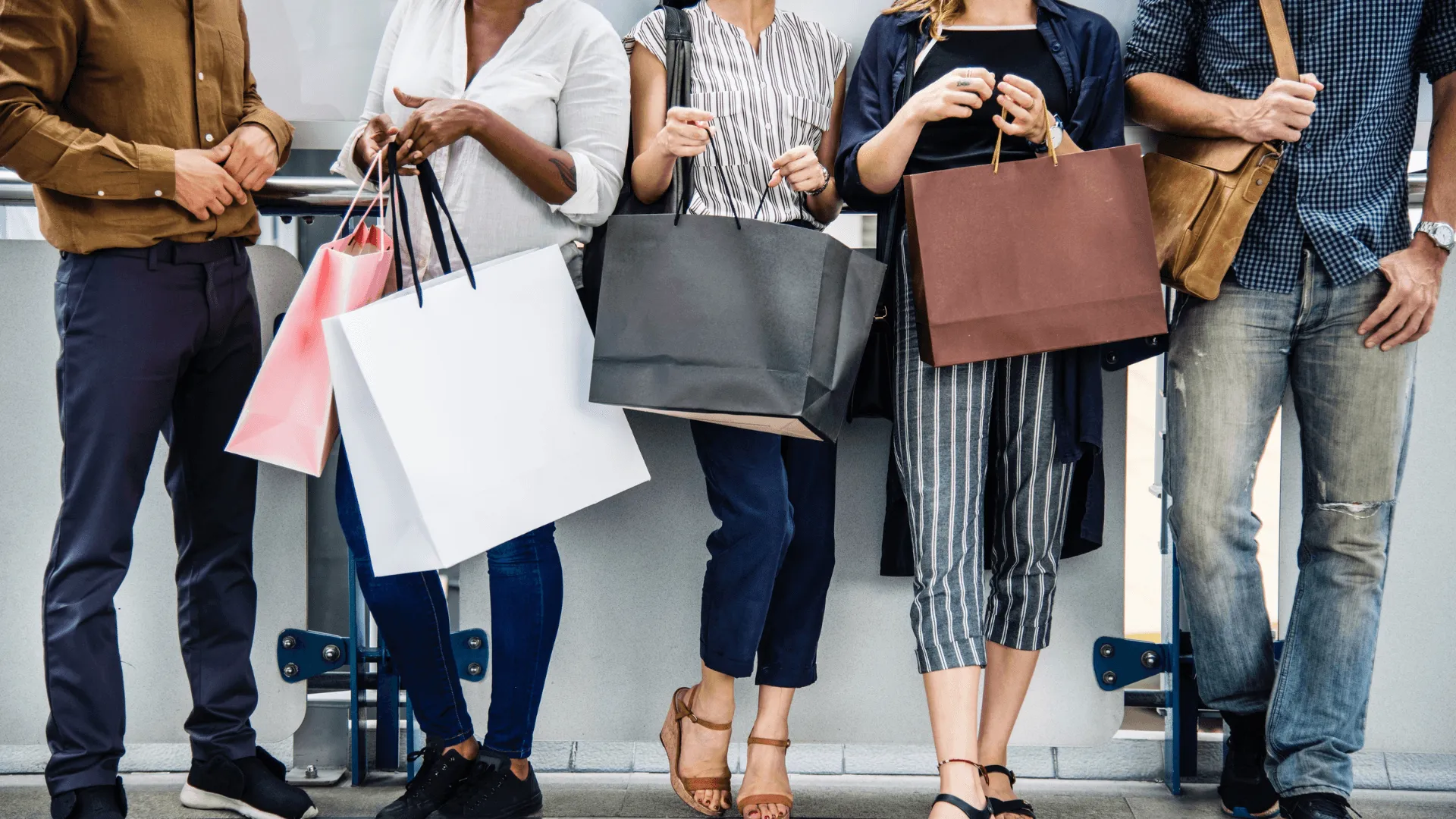 A neck down shot of a group of people, all in a line, holding shopping bags