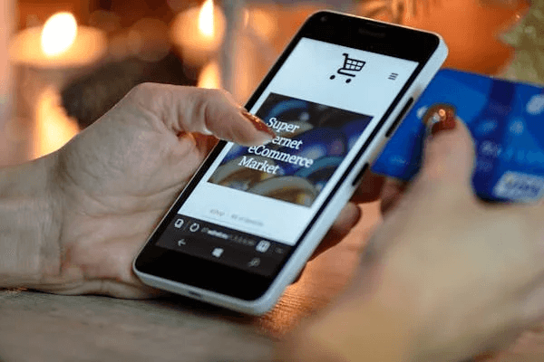 Hand holding smartphone with e-commerce site and credit card.