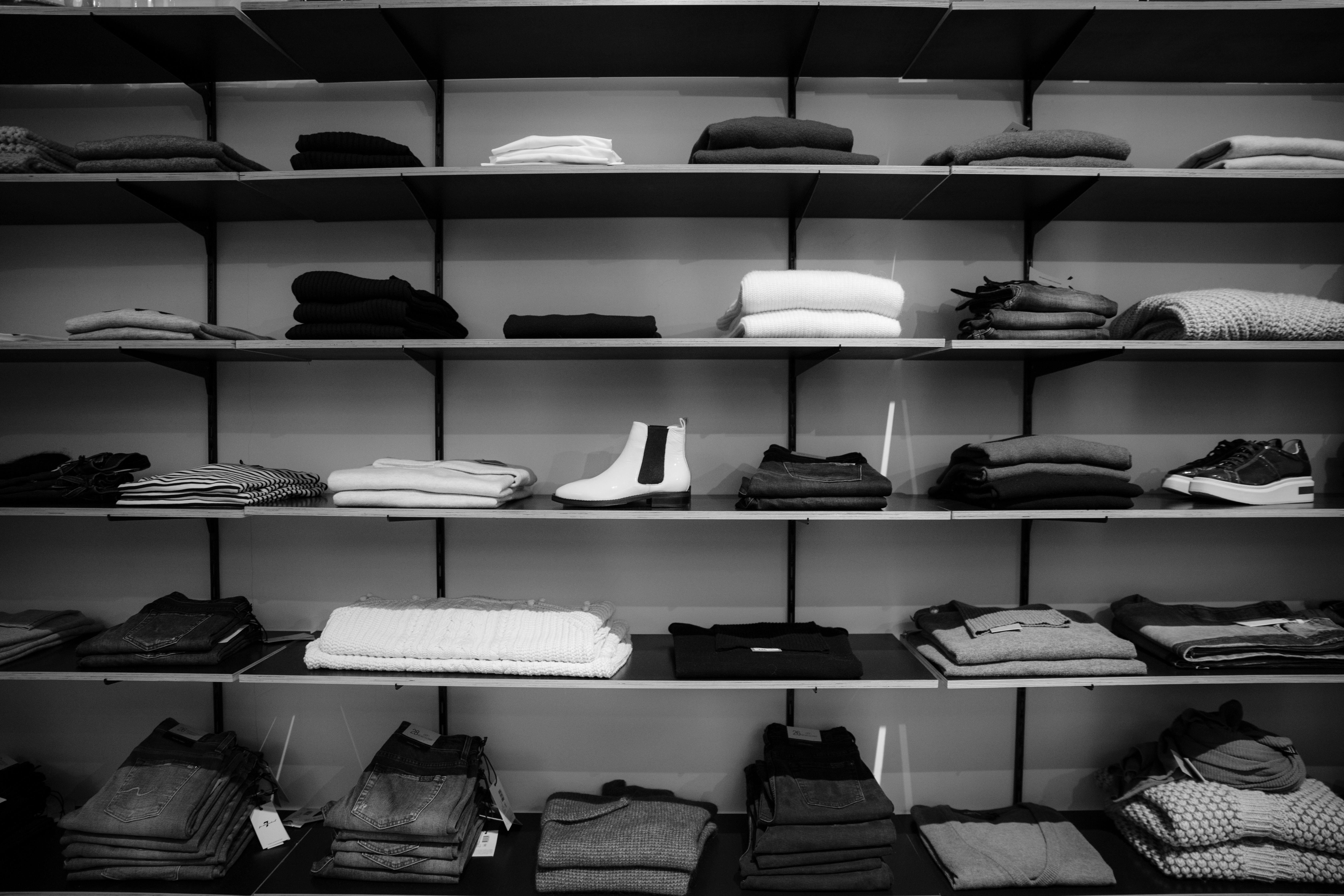 Black and white image of neatly folded clothing and shoes displayed on shelves in a retail store.