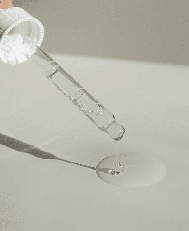 "Close-up of a glass dropper releasing a clear liquid, symbolizing precision and quality in skincare or cosmetic products."