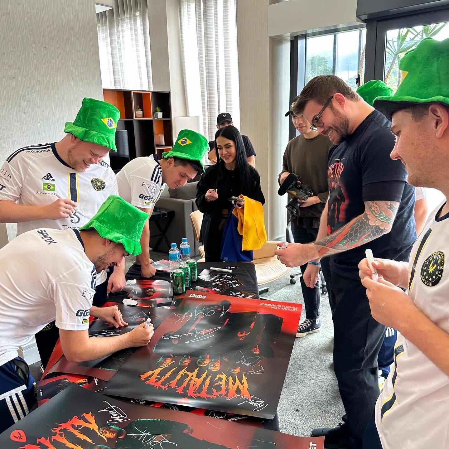 Visuel du Projet Metality : l'équipe Metality signe des autographes sur des affiches tout en portant des chapeaux de seau aux couleurs du Brésil.