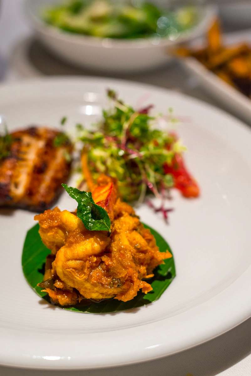A plated dish featuring fried orange shrimp with a green leaf and basil garnish next to grilled vegetables on a white plate.