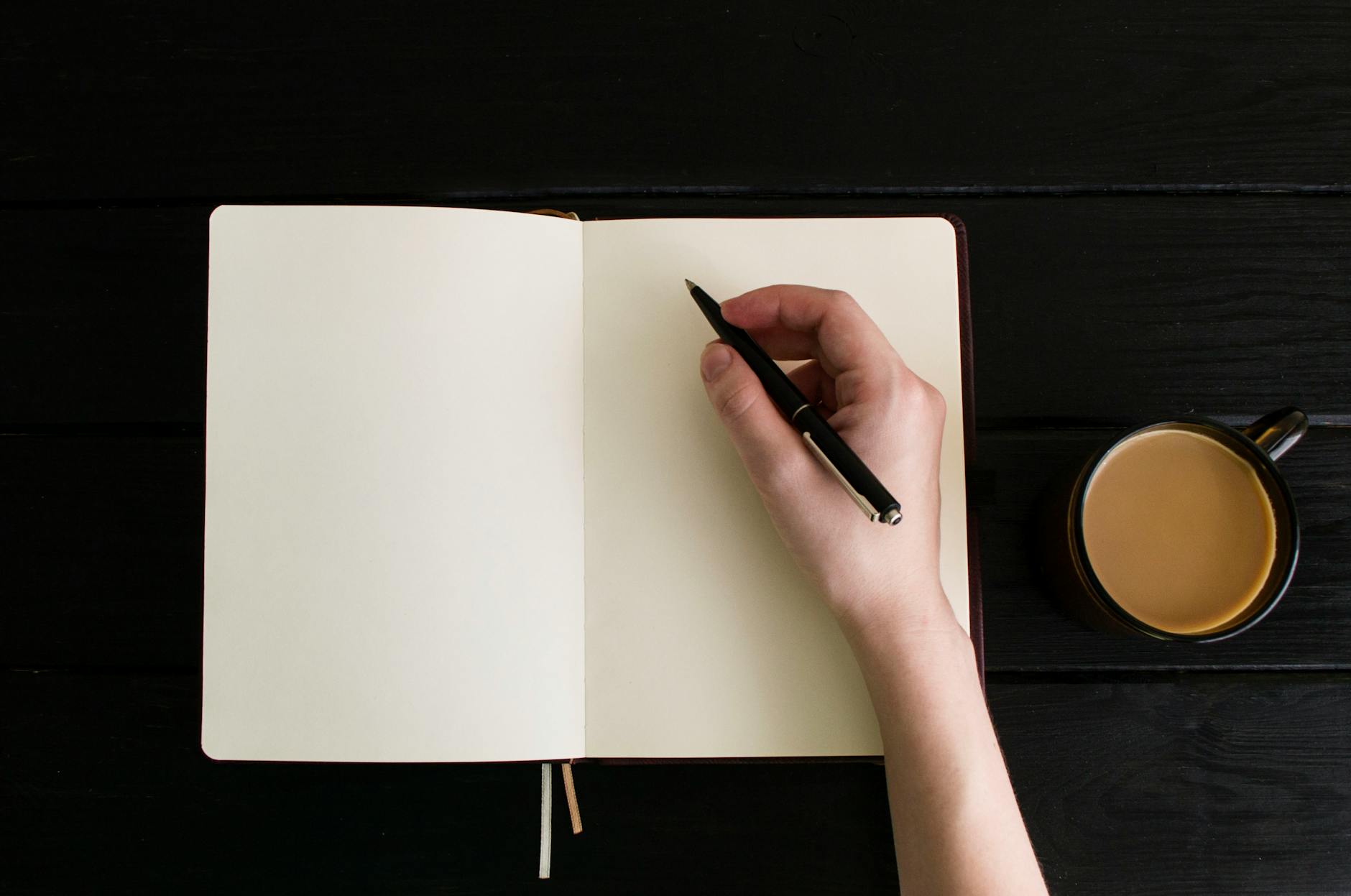 Top-down view of a wooden desk featuring a laptop, an open paper planner, colorful pens, and a cup of coffee.