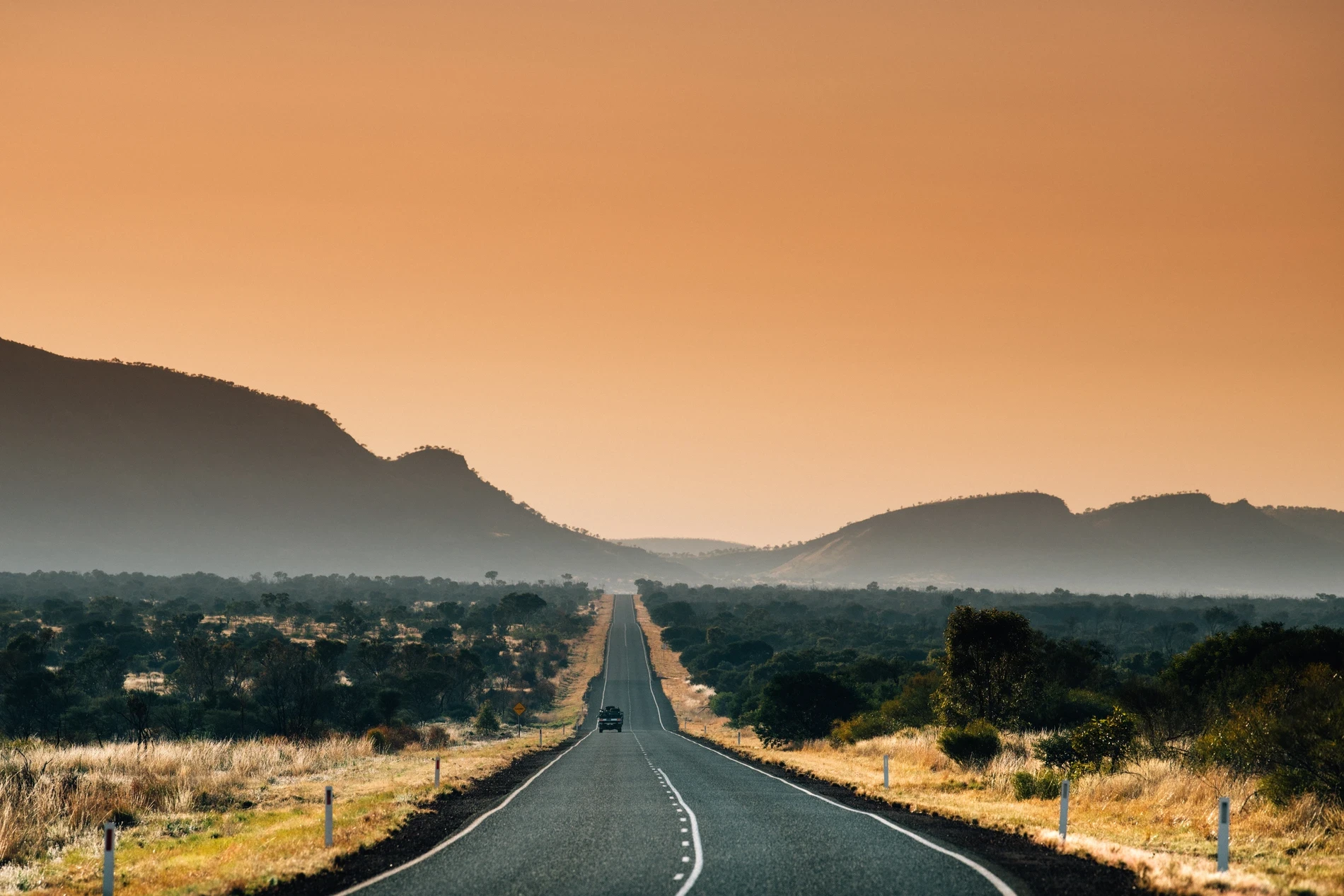 A straight highway running toward hills through dry country in hazy light
