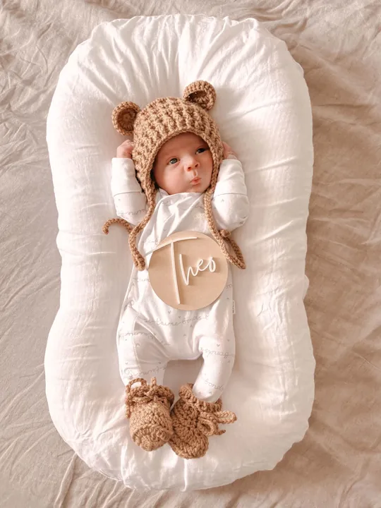 Baby in a knitted bear bonnet resting on a white cushion